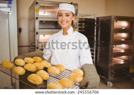 Baker smiling at camera holding rack of rolls in a commercial kitchen