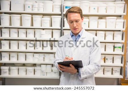Handsome pharmacist writing on clipboard at the hospital pharmacy
