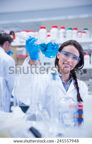 Portrait of a smiling chemist holding a beaker of blue liquid in lab