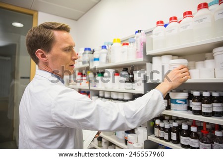 Handsome pharmacist taking medicine from shelf at the hospital pharmacy