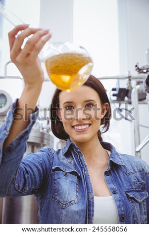 Woman looking at camera while holding beaker of beer in the factory