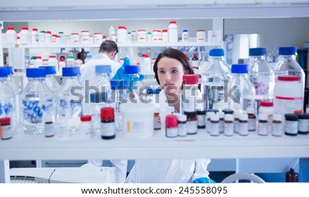 Young chemist picking up the bottles on the shelf in lab