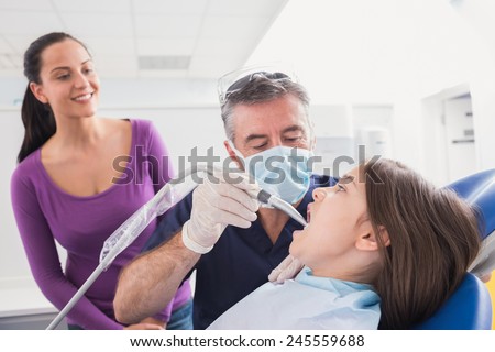 Pediatric dentist examining young patient with a suction tube in dental clinic