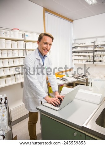 Happy pharmacist using his laptop at the hospital pharmacy