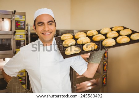 Baker smiling at camera holding tray of rolls in a commercial kitchen
