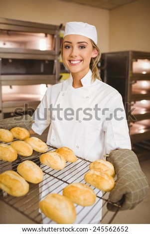 Baker smiling at camera holding rack of rolls in a commercial kitchen