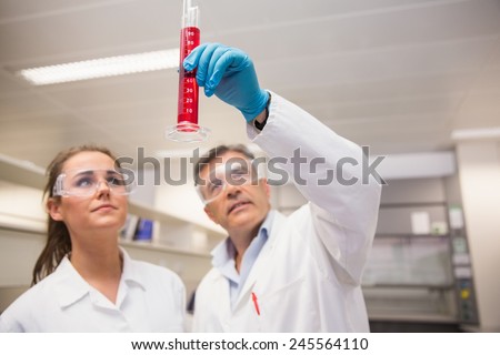 Pharmacists looking at beaker of red liquid at the laboratory