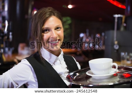 Happy barmaid holding tray with coffee in a bar