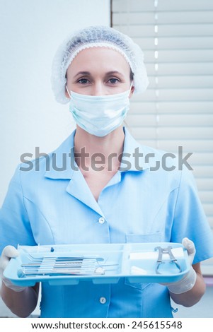 Portrait of female dentist in surgical mask holding tray of tools