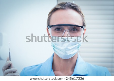 Portrait of female dentist in surgical mask and safety glasses holding injection