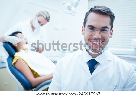 Portrait of smiling male dentist with assistant examining womans teeth in the dentists chair