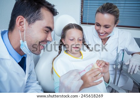 Male dentist with assistant teaching girl how to brush teeth in the dentists chair
