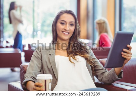 Smiling girl using digital tablet and holding disposable cup in library