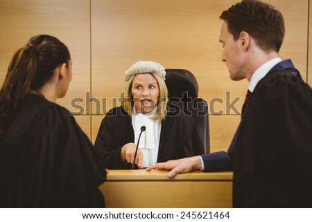 Judge wearing a dress and a wig speaking with lawyers in the court room