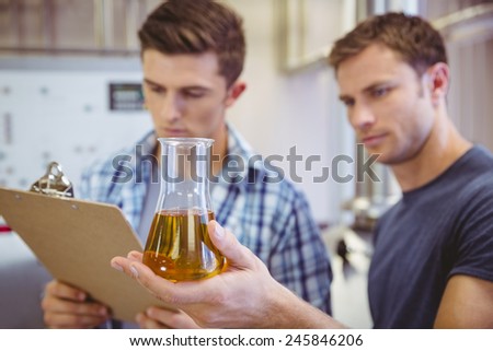 Two men looking at the beaker with beer in the factory
