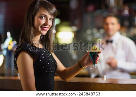 Pretty brunette smiling at camera with cocktail in a bar
