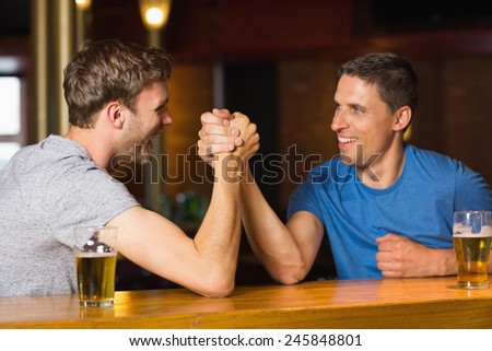 Happy friend arm wrestling each other in a bar