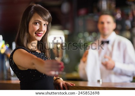 Pretty brunette smiling at camera with champagne in a bar