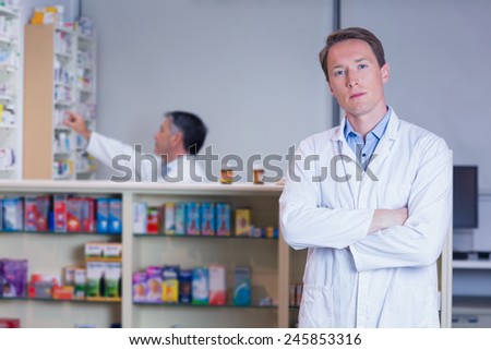 Unsmiling pharmacist standing with arms crossed in the pharmacy