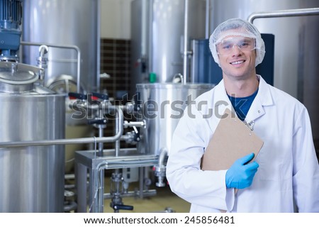 Smiling scientist looking at camera holding a clipboard in the factory