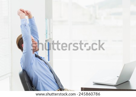 Focused businessman stretching at his desk in his office
