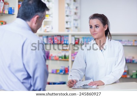 Trainee writing prescription in front of a customer in the pharmacy