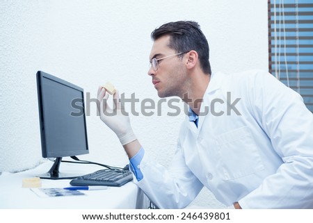 Male dentist holding mouth model besides computer