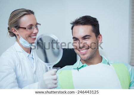 Smiling young man looking at mirror in the dentists chair