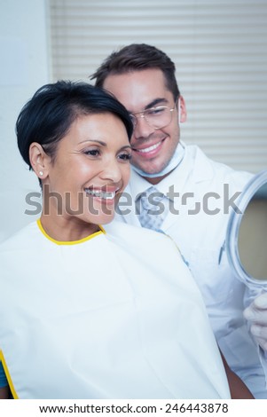 Smiling young woman looking at mirror in the dentists chair
