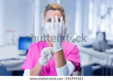 Dentist in pink scrubs putting on surgical gloves at the dental clinic