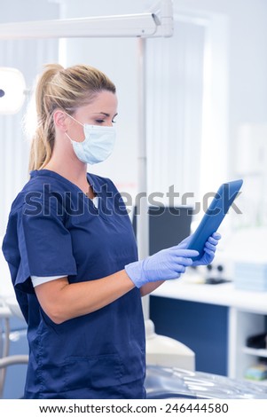 Dentist in mask and blue scrubs using her tablet at the dental clinic