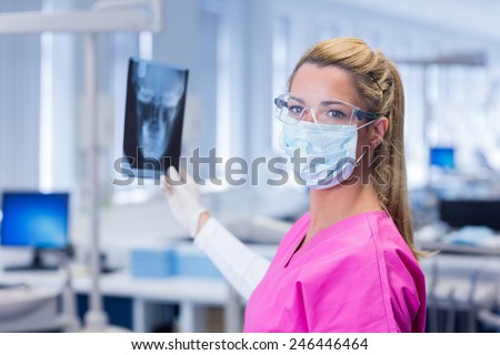Dentist in pink scrubs holding an x-ray and looking at camera at the dental clinic