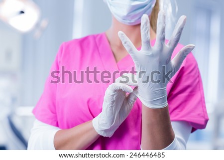 Dentist in pink scrubs putting on surgical gloves at the dental clinic