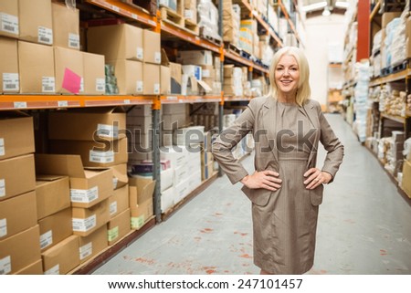 Smiling manager placing her hands on her hips in a large warehouse