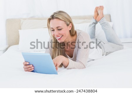 Smiling blonde using tablet on the bed in hotel room