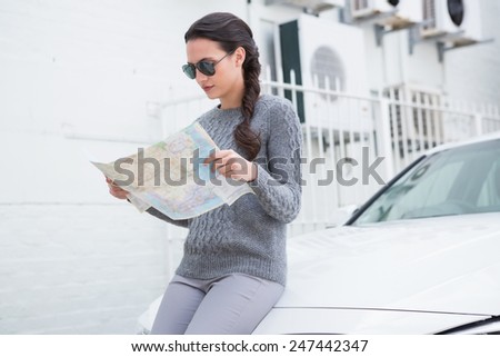 Woman wearing sunglasses reading map beside her car in a car park