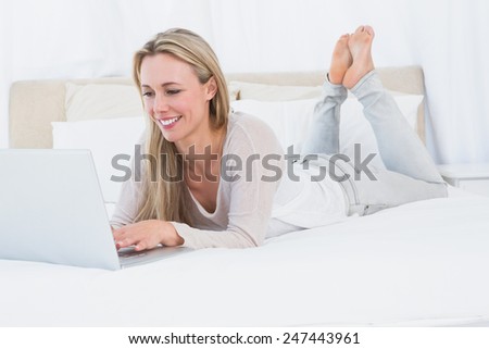 Smiling blonde typing on laptop on the bed in hotel room