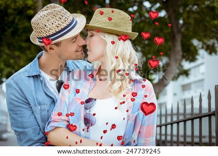 Hip young couple kissing by railings against red heart balloons floating