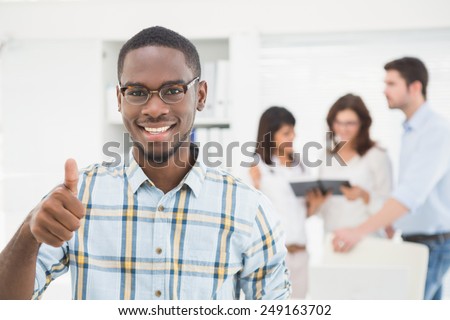 Positive businessman with thumbs up with his colleagues behind him