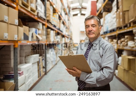 Smiling warehouse manager holding a clipboard in a large warehouse