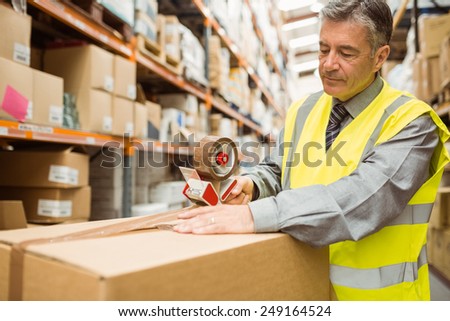 Warehouse worker sealing cardboard boxes for shipping in a large warehouse