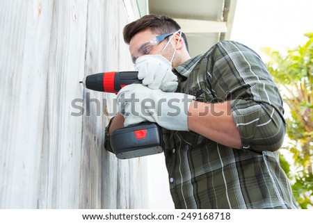 Male carpenter using drill machine on wooden cabin