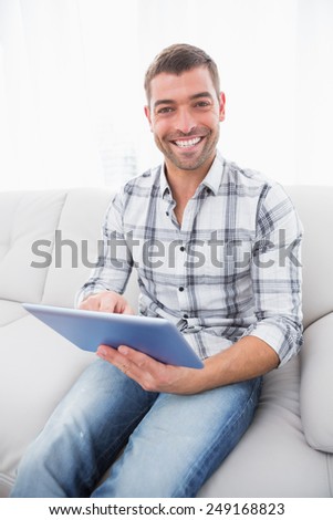 A smiling man sitting in the sofa with a tablet
