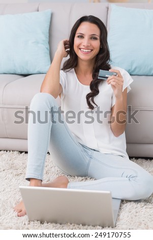 Pretty brunette shopping online with laptop at home in the living room