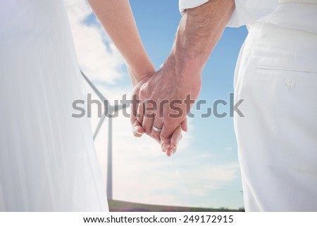 Bride and groom holding hands close up against windmill spinning over a green field