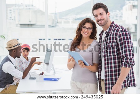 Smiling teamwork standing and using tablet with colleagues behind them