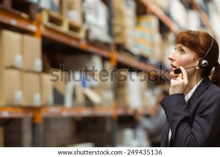 Pretty businesswoman speaking in a headset in a large warehouse