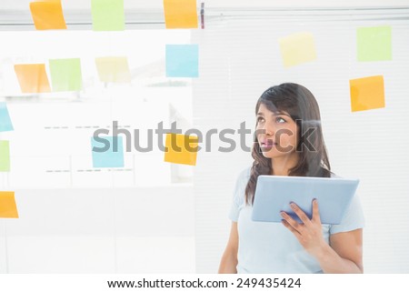 Businesswoman holding tablet and reading sticky notes in the office