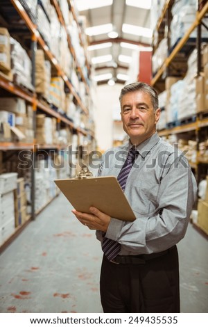 Smiling warehouse manager holding a clipboard in a large warehouse