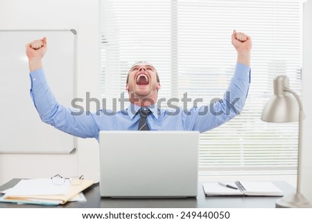 Excited businessman with arms up cheering in his office
